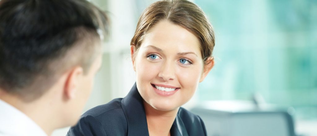 woman at a meeting smiling while talking to a man at a desk